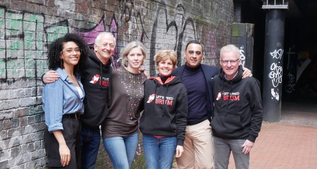 Let's Feed Brum Trustees stand side-by-side on a red brick canal path in Birmingham. In the background is a neutral brick wall covered in street art.